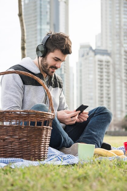 Smiling young man sitting in the park listening music on cell phone