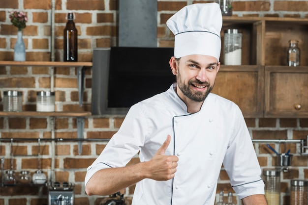 Smiling young man standing in kitchen showing thumb up sign