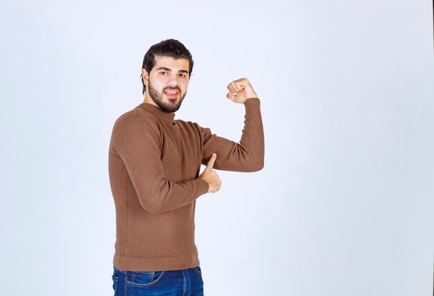 Smiling young man in sweater showing bicep and looking at camera. High quality photo