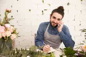 Free photo smiling young man taking order on mobile phone in the florist shop