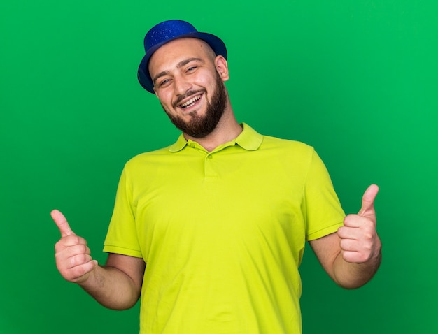 Smiling young man wearing blue party hat showing thumbs up 