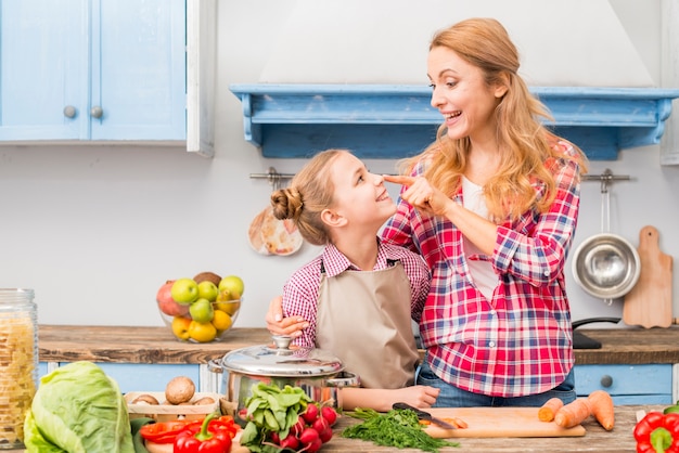 Smiling young mother touching her daughter's nose with finger in the kitchen