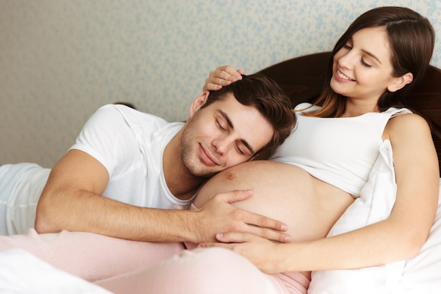 Smiling young pregnant wife lying in bed with her husband