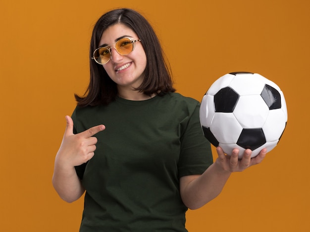 Free Photo smiling young pretty caucasian girl in sun glasses holding and pointing at ball