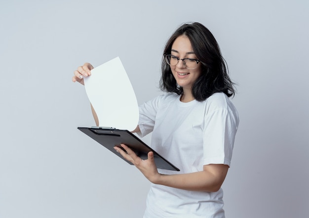 Free Photo smiling young pretty caucasian girl wearing glasses holding and looking at clipboard isolated on white background