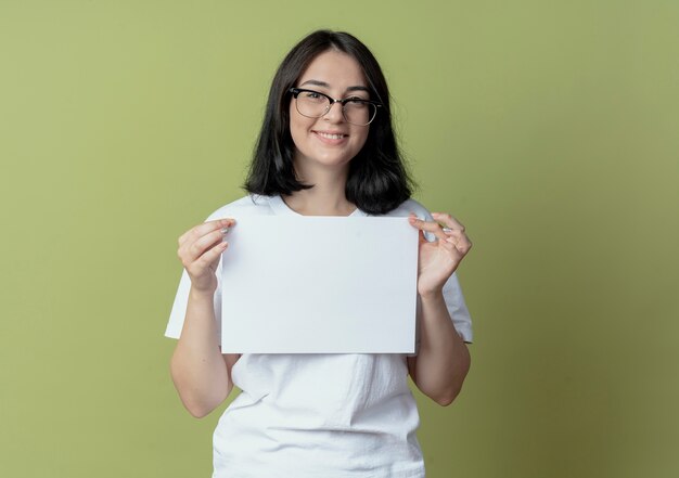 Smiling young pretty caucasian girl wearing glasses holding paper isolated on olive green background with copy space