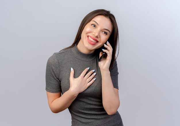 Smiling young pretty woman talking on phone looking straight putting hand on chest isolated on white background with copy space