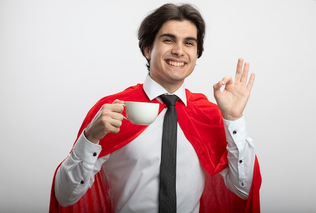 Smiling young superhero guy looking at camera wearing tie holding cup of coffee