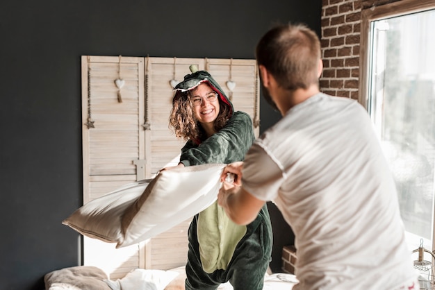 Smiling young woman doing pillow fight with her husband at home