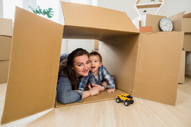 Smiling young woman embracing her baby son inside the moving cardboard box