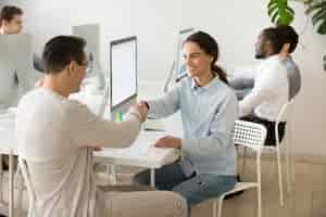 Free photo smiling young woman handshaking satisfied client making deal in office