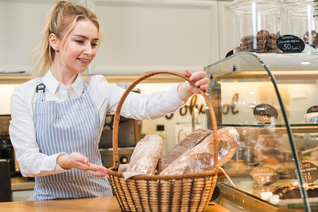 Free Photo smiling young woman holding basket of baguette in the coffee shop