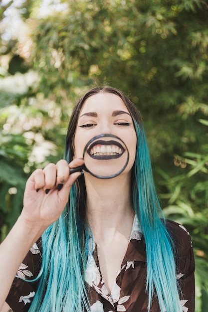 Smiling young woman holding magnifying glass over her face