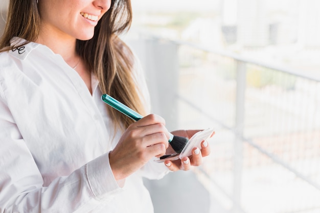 Smiling young woman holding makeup brush and compact powder