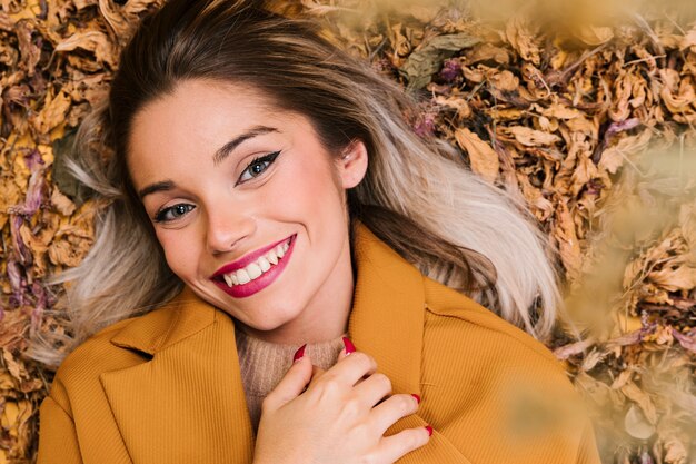 Smiling young woman looking at camera lying on dry leaves