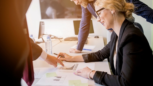 Smiling young woman looking at graph pointed by her colleague on table