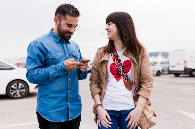 Smiling young woman looking at man using cell phone at street