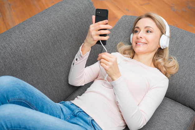 Smiling young woman looking at mobile phone listening music on headphone