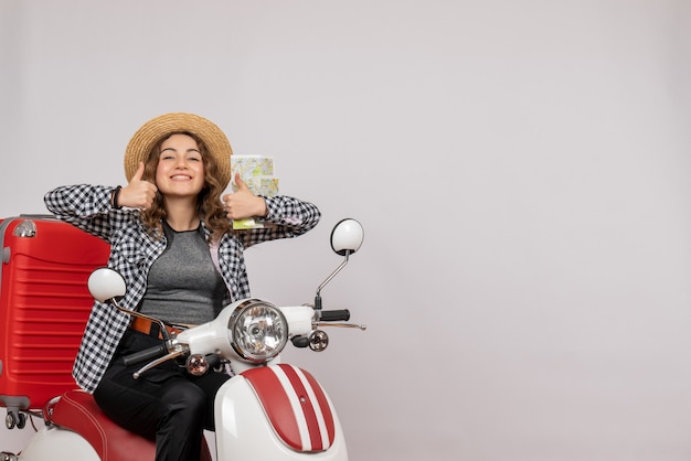 smiling young woman on moped holding card making thumbs up sign on grey