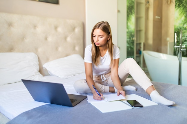 Free photo smiling young woman paying her bills online with laptop in bedroom at home