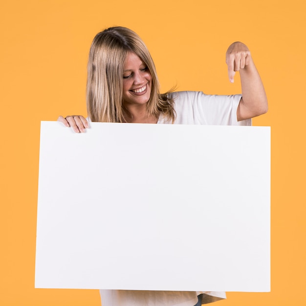 Smiling young woman pointing index finger at white blank placard