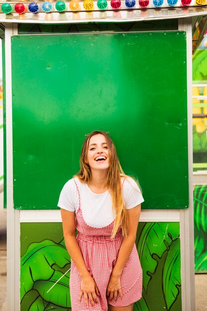 Smiling young woman posing in front of green wall at amusement park