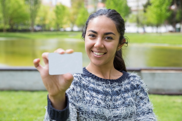 Smiling young woman showing blank business card in city park