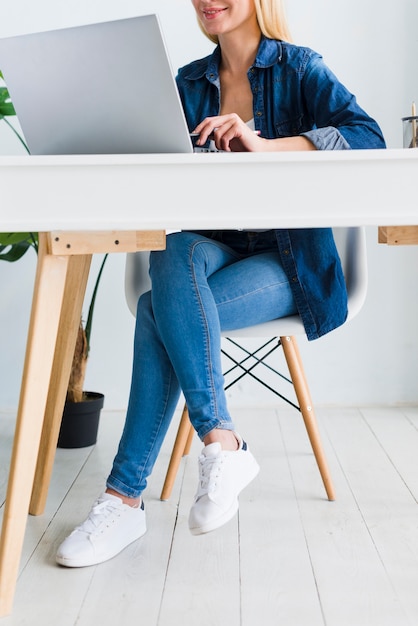 Free photo smiling young woman sitting in chair near laptop