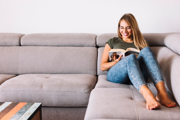 Smiling young woman sitting on couch reading book