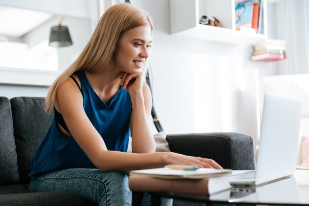 Smiling young woman sitting and working with laptop at home