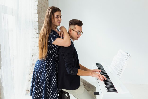 Smiling young woman standing behind the man playing the piano