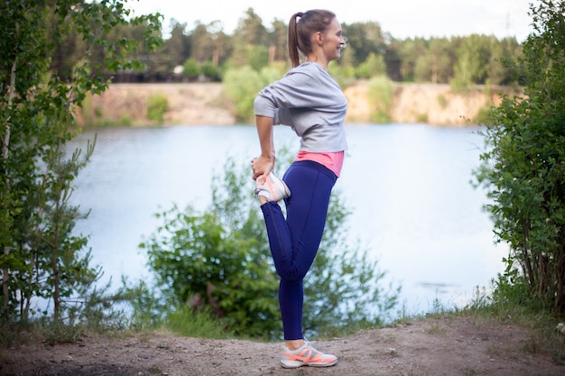 Smiling young woman stretching leg before jogging