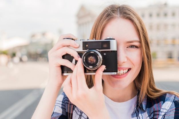 Free photo smiling young woman taking picture with camera at outdoors