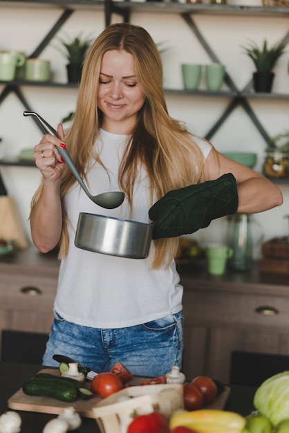 Free photo smiling young woman tasting food standing behind the kitchen counter