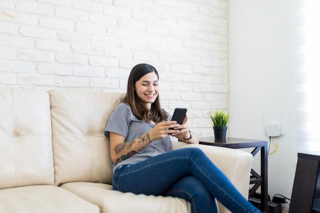 Smiling young woman text messaging on mobile phone at home