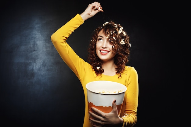 Free photo smiling young woman throwing popcorn looking up with wide smile