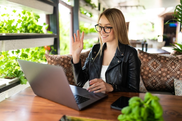 Smiling young woman using laptop and making video call in cafe.