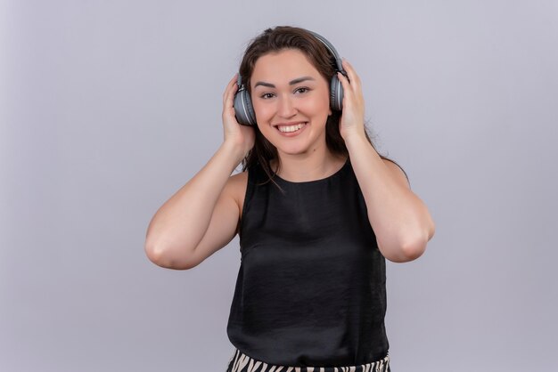 Smiling young woman wearing black undershirt in headphones on white wall