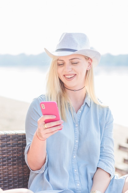 Free photo smiling young woman wearing hat holding mobile phone