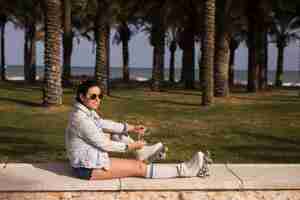 Free photo smiling young woman wearing sunglasses tying lace of roller skate