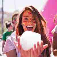 Free photo smiling young woman with holi color on her face holding foam in hand looking at camera