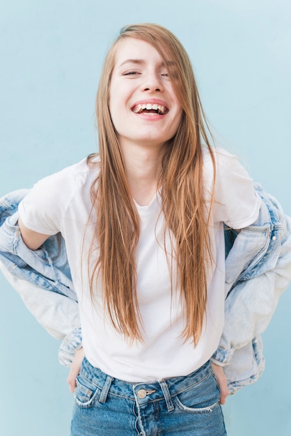 Smiling young woman with long blonde hair standing on blue backdrop