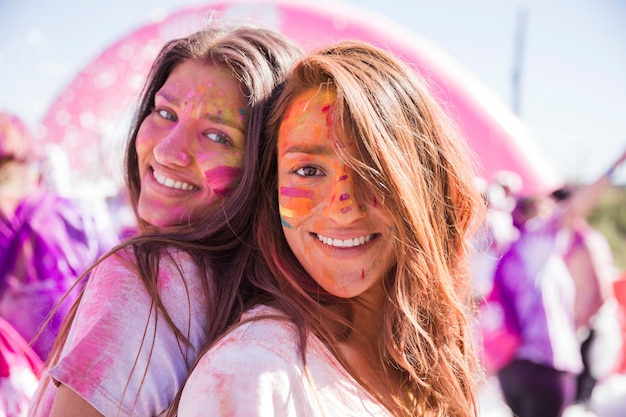 Free Photo smiling young women with holi color on their face standing back to back