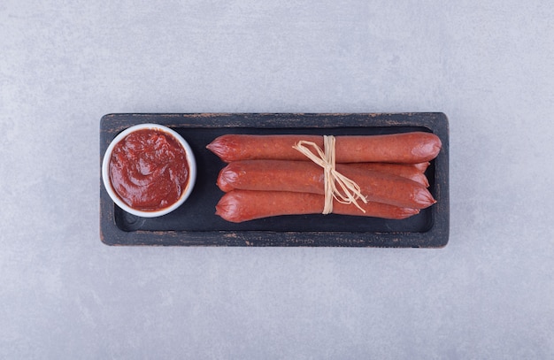 Smoked sausages and ketchup on dark plate. 