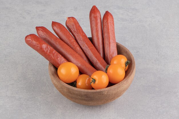 Smoked sausages and tomatoes in wooden bowl.