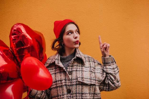 Free photo snapshot of shorthaired woman in red hat with heartshaped balloons girl in tweed jacket has idea what to present for valentines day