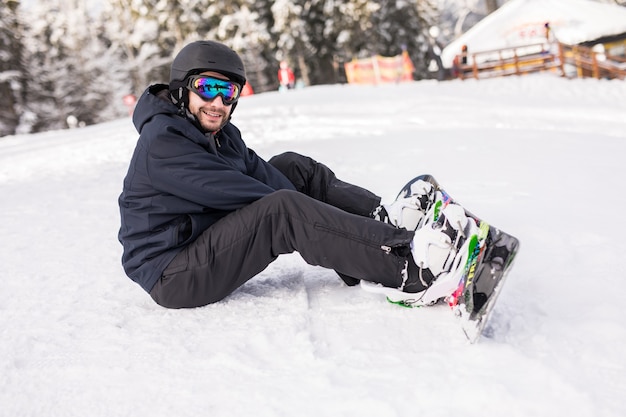 Snowboarder sits high in the mountains on the edge of the slope and looks at camera before ride