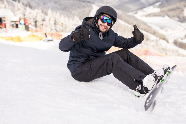 Snowboarder sits high in the mountains on the edge of the slope and looks at camera before ride