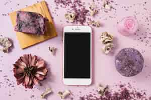 Free photo soap bar; herbal body scrub; dried flower and smartphone on pink background