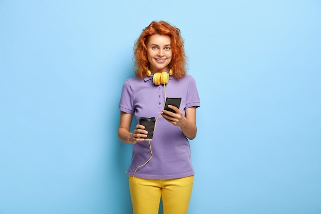 Free Photo sociable communicative girl sends text messages via smart phone, drinks coffee from paper cup